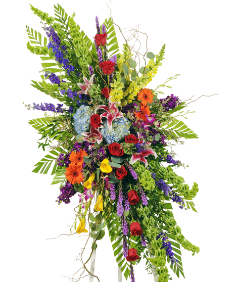 A spray of bright roses, hydrangeas, snapdragons, lilies, and gerbera daisies, mixed with greenery. Displayed on an easel against a white background.