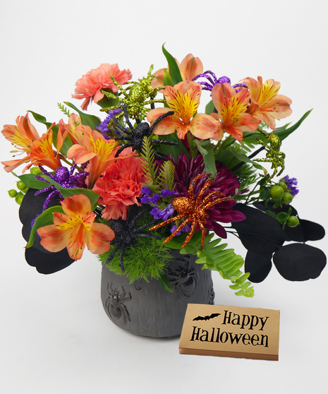 A Halloween-themed floral arrangement with bright orange, yellow, and purple flowers accented by sparkly green, purple, and orange glitter spiders.