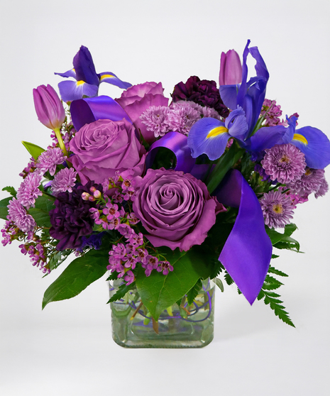 Bouquet of purple flowers in a glass vase adorned with ribbon and wire accent