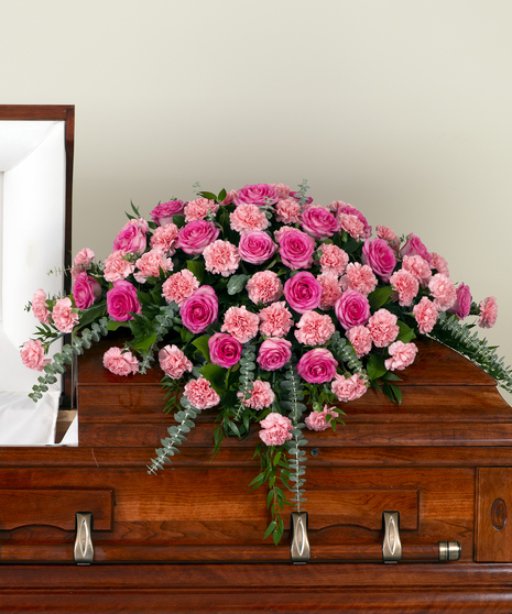 A large spray of roses and carnations, mixed with greenery. Displayed on top of a closed casket.