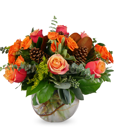  fresh flower arrangement in a glass bubble bowl featuring cherry brandy roses, spray roses, solidago, magnolia, eucalyptus, and pinecones, for a seasonal sympathy tribute.