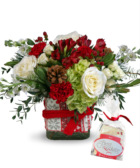 Holiday arrangement of red carnations, white roses, and greenery in a vase wrapped with a festive ribbon.